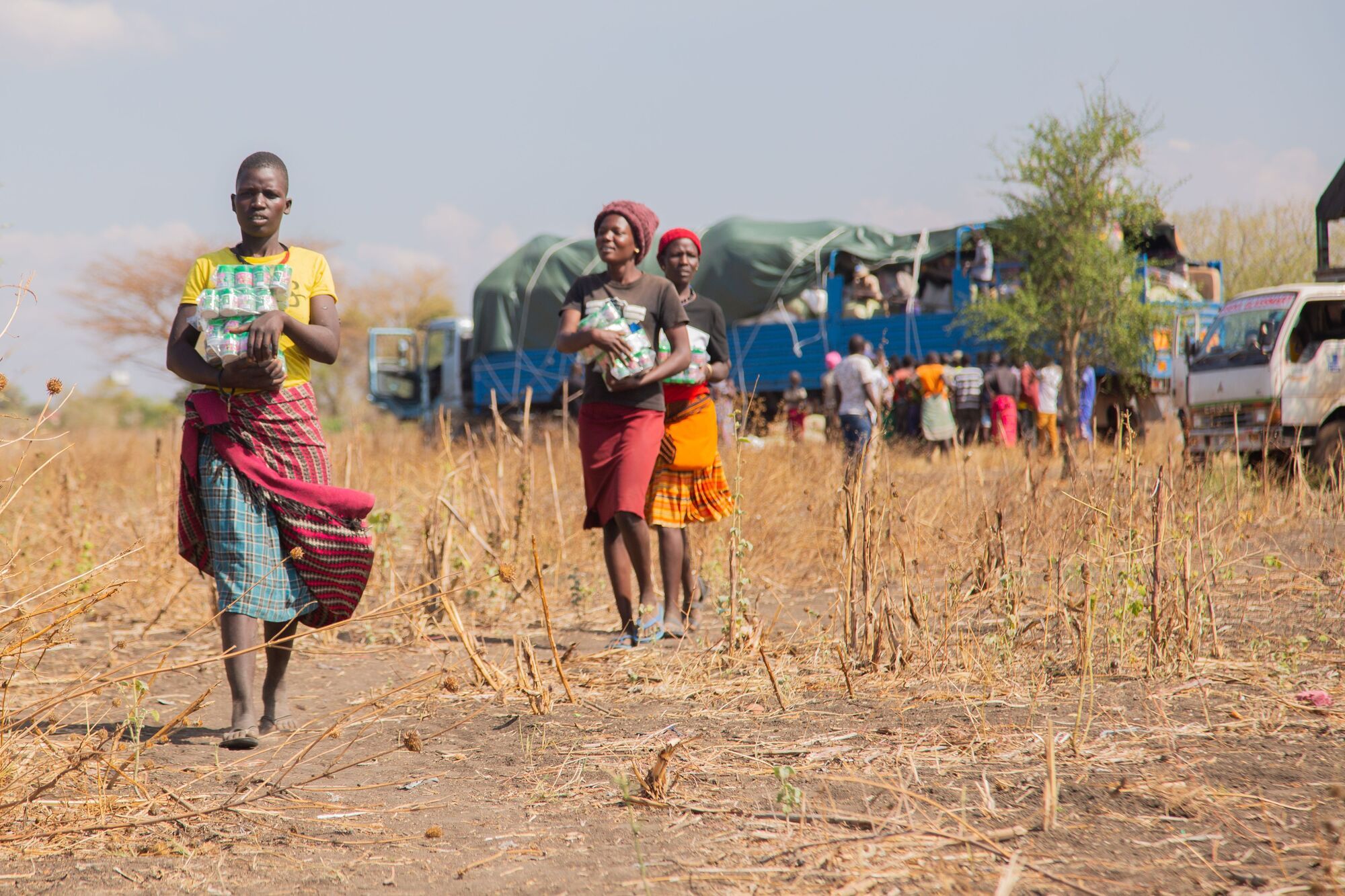 Women carrying relief supplies away from aid trucks at a rural distribution point